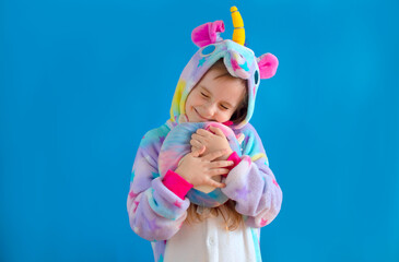 baby girl in a cozy blue unicorn costume poses in the studio on a blue isolated background. Place for text.