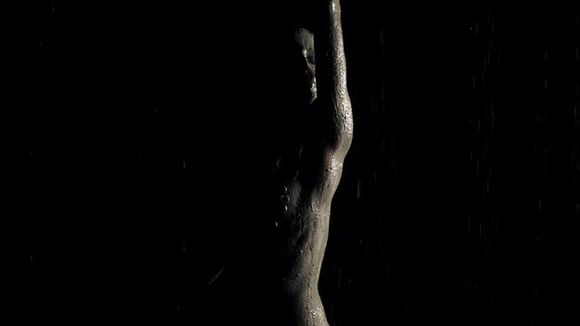 sexy lady covered by mud is dancing and singing in shower in darkness