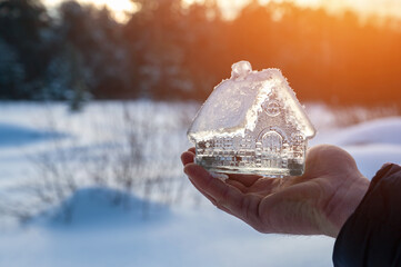 Close-up man's hand holding small glass, crystal house against background winter landscape. Artistically colored  tinted photo. Concept dream home, real estate business. Take out mortgage. Copy space