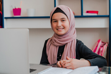 Muslim girl student smiling while learning for school at home desk using a laptop.