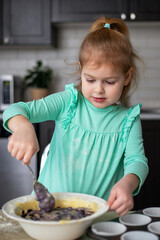 Little girl mixing ingredients for homemade blueberry muffins. Small child cooking in kitchen.