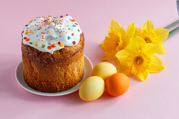 Easter cake, eggs and daffodil flowers on pink background.