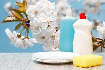 Fototapeta na wymiar Bottles of dishwashing liquid, plates and sponge on natural background.
