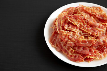 Crispy Fried Bacon on a white plate on a black background, low angle view. Copy space.