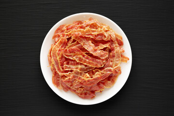 Crispy Fried Bacon on a white plate on a black background, top view. Flat lay, overhead, from above.