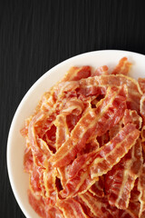 Crispy Fried Bacon on a white plate on a black surface, top view. Flat lay, overhead, from above. Copy space.