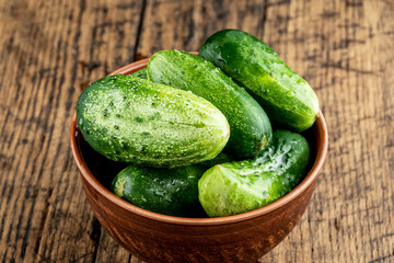 brown bowl of fresh domestic small cucumbers over wooden background. rustic cucumber close up
