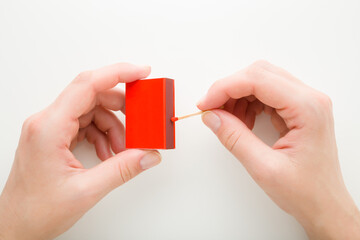 Young adult woman hands holding red box and igniting match stick on white background. Closeup....