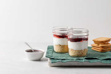 Dessert with yogurt, cookies, jam in a glass jar on green napkin and grey background