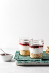 Dessert with yogurt, cookies, jam in a glass jar on green napkin and grey background