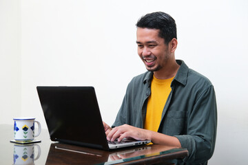 Adult Asian man smiling happy when typing on his laptop