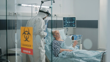 Doctor consulting woman infected with coronavirus in bed. Medic doing checkup visit for aged...