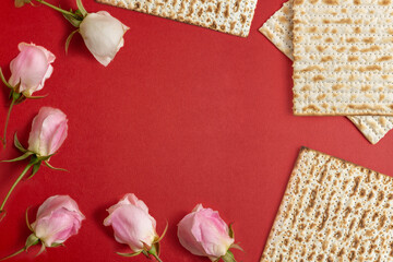 Matzah and rose flowers for Jewish holiday Pesach on red background with copy space.