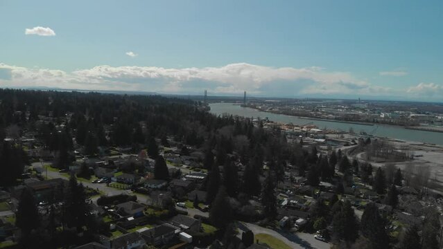 Scenic view of Delta BC on the edge of the Fraser river with the Alex Fraser bridge in the background Bright day blue sky clouds Aerial Wide approaching descending tracking bridge on background