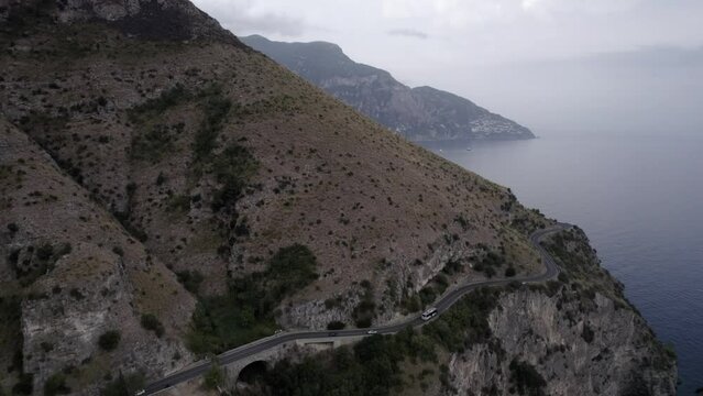 Drone video over the Amalfi Coast at the height of Positano flying the cliff with frontal plane advancing and discovering Positano in the distance.
Cloudy sky shows boats, a boat sailing and vehicles.