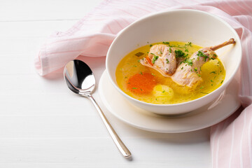 Chicken soup with vegetables in white bowl on wooden table