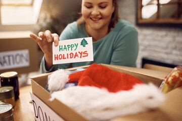 Close-up of woman adding greeting card while packing donation boxes for holidays.