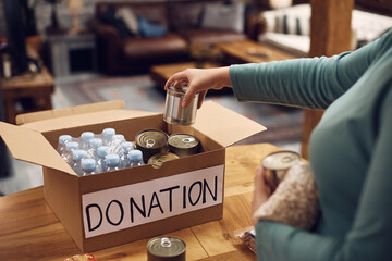 Close up of volunteer packs donated canned food in cardboard box.