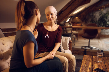Smiling woman with breast cancer talks to her female friend at home.