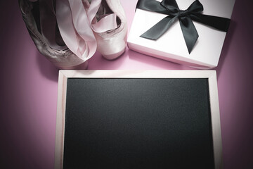 Pink ballet shoes with long ribbons lying on a pink background. Pink gift box with black...
