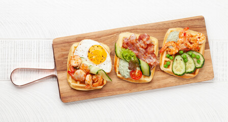 Breakfast waffles with fried eggs, salmon, cucumber and prawns