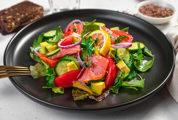 Salad with salmon, avocado and vegetables on a gray background. Side view, close-up.