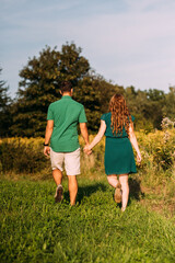 Junges Paar mit grünen Sachen Hand in Hand laufend in schöner grüner Natur von hinten