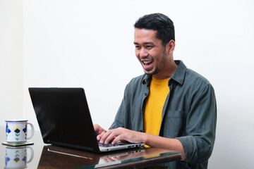 Adult Asian man showing excited expression when typing on his laptop
