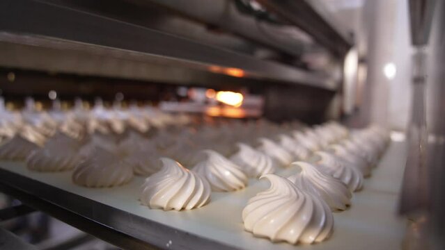 Conveyor belt moving slowly carrying freshly-made marshmallows. Creamy sweets manufacturing at food factory. Close up. Sweet backdrop.