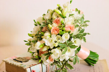 Bouquet of freesia flower, roses and light leaves and book on light pink background. Handle of bouquet is decorated with peach colored ribbon. Bunch of flowers, vintage style, front view.