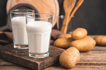 Two glasses of potato milk with raw potatoes on a brown background.