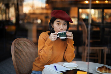 Beautiful Chinese woman drinking coffee in cafe. Young smiling woman enjoy in restaurant..