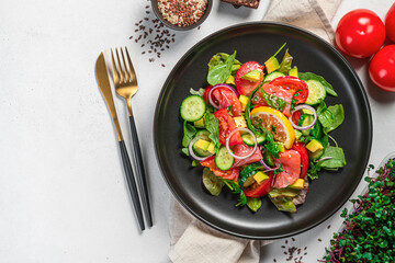 Healthy salad with salmon, avocado, fresh herbs, flax and sesame seeds and micro-greenery on a gray background.