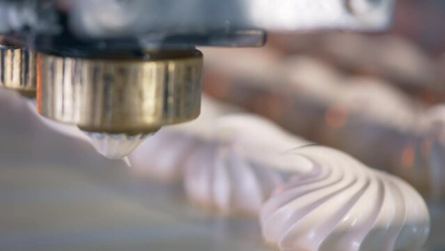 Little rotating nozzle letting out creamy stuff on conveyor belt. Close up. Vanilla desserts are squeezed in little distance from each other. Sweets manufacturing at confectionary factory.