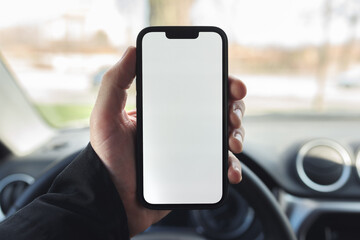 Smartphone with blank white screen in hands of male driver over car steering wheel