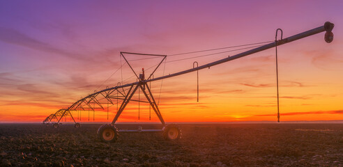 Fototapeta na wymiar Lateral move agricultural irrigation system on plowed field in sunset