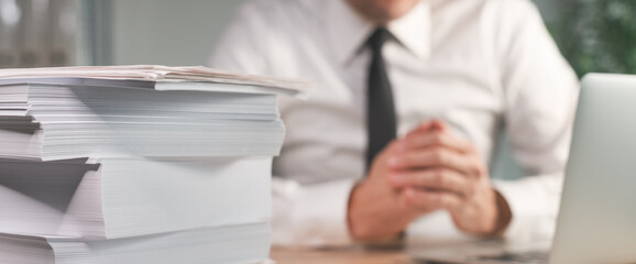 To much paperwork, businessman at the desk with piled business paper to be archived