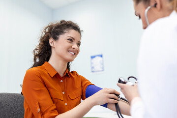 Nurse measuring blood pressure of a woman patient during an examination in the clinic. Doctor...