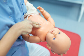 Woman performing CPR on baby training doll with one hand compression. First Aid Training - Cardiopulmonary resuscitation. First aid course on cpr dummy.