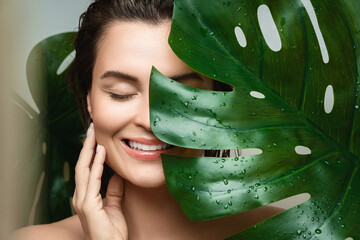 Young woman with a smooth skin holding Monstera deliciosa plant leaf