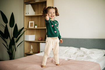 A little girl stands on the bed and shows the class with her fingers