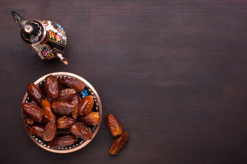Plate with dates, coffee pot  on dark brown wooden table. Ramadan background.  Top view.