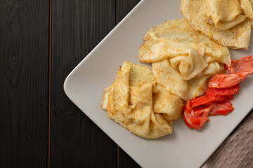 Thin Russian pancakes and pieces of salted red fish are laid out on a gray rectangular plate