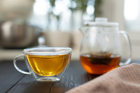On a wooden table there is a teapot with freshly brewed natural green tea, a double-walled glass mug with tea and a slice of lemon