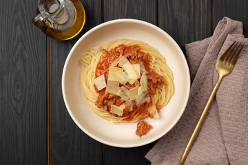 Spaghetti pasta with bolognese sauce, parmesan cheese on a wooden table, next to a golden fork and a bottle of olive oil, flat lay, open space