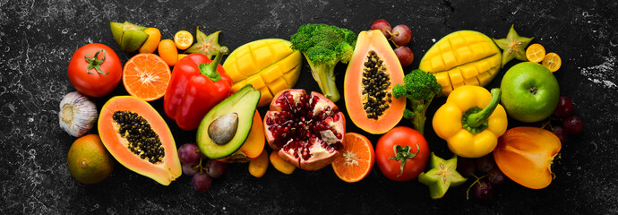 Vegetables and fruits, healthy food. Fruits and vegetables on black stone background. Tropical fruits. Top view. Free space for your text.