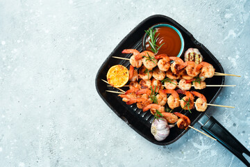 Seafood. Grilled shrimp on skewers with lemon and garlic in a pan. On a stone background. Top view.