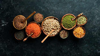 Obraz na płótnie Canvas Legumes, a set consisting of different types of beans, lentils and peas, rice and buckwheat on a black background, top view. The concept of healthy and nutritious food