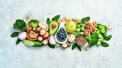 Vegetables and fruits: avocado, green broccoli, nuts, mushrooms, berries and green apples, quinoa. Healthy food. On a gray stone background. Top view.