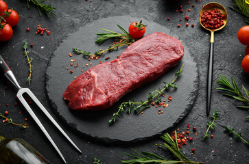 Raw sirloin steak with thyme, rosemary and spices. Top view. Flat lay top view on black stone cutting table.